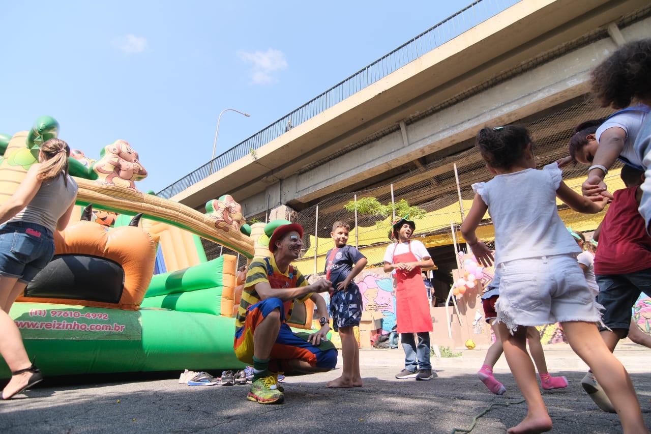 Brinquedos infláveis ao fundo, palhaços e atrações para crianças e público infantil durante a diversão